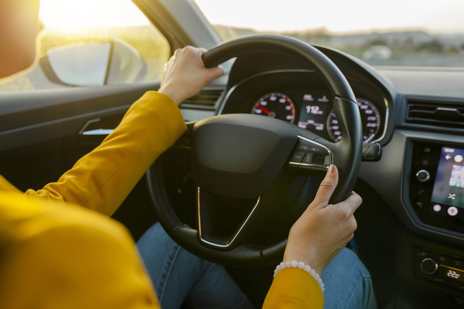 Close-up female hands in yellow suit driving car outside city